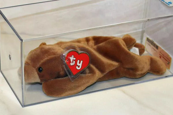 A brown Beanie Baby in a clear display case with its heart-shaped Ty hang tag in a protector.