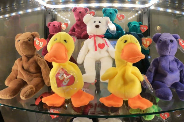 A lit display case of early Beanie Babies, including Teddy bears in several colors, a white Valentino bear and two Quackers ducks