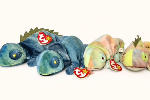 Four Iggy the Iguana Beanie Baby variations side by side: two blue toys and two tie-dye pastel toys with Ty heart tags