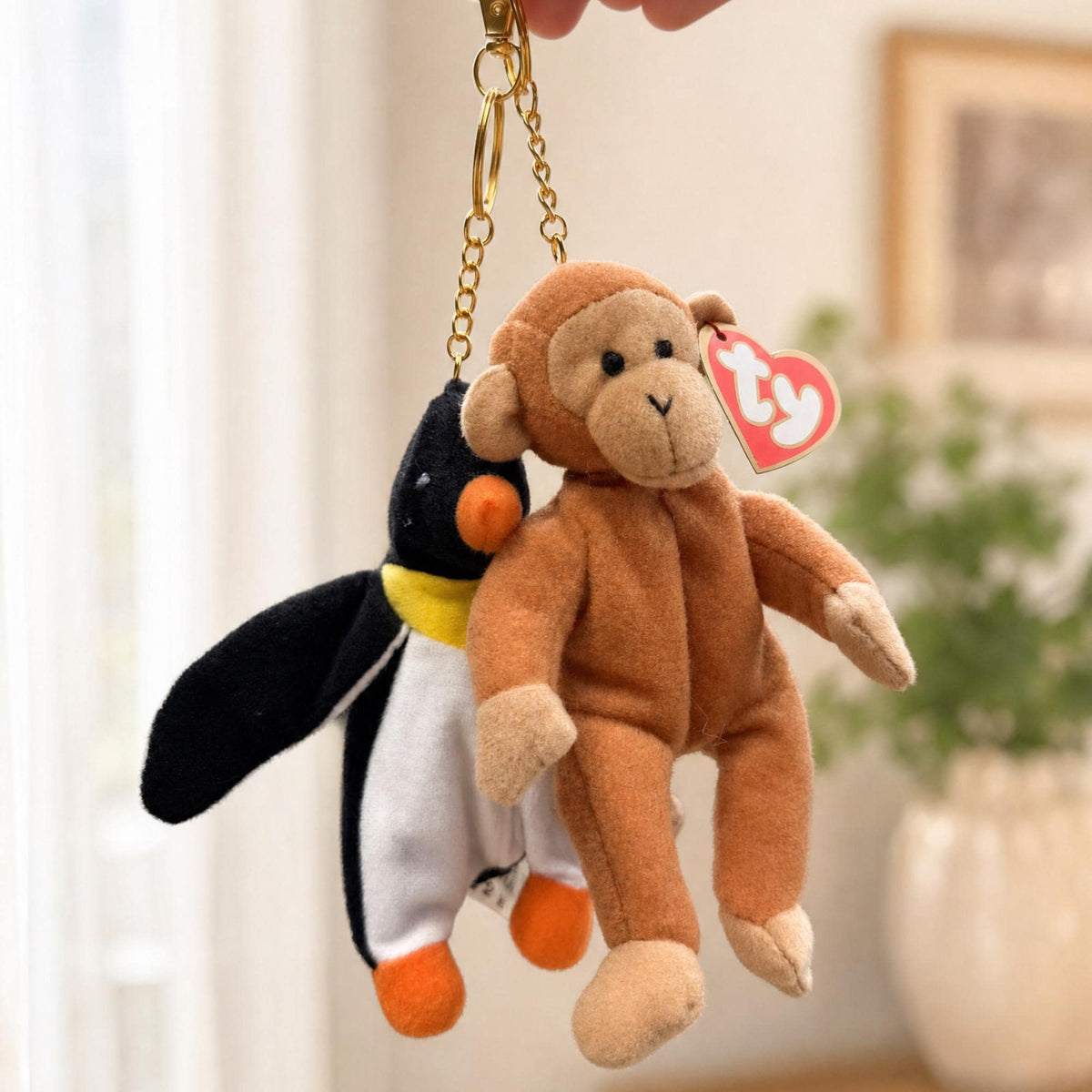 Two Teenie Beanie Baby bag charms, a penguin and a monkey, held up on their gold clips