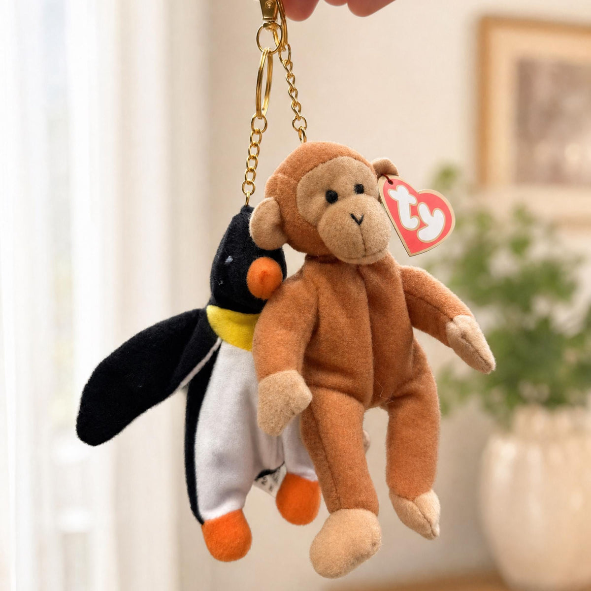Two Teenie Beanie Baby bag charms, a penguin and a monkey, held up on their gold clips