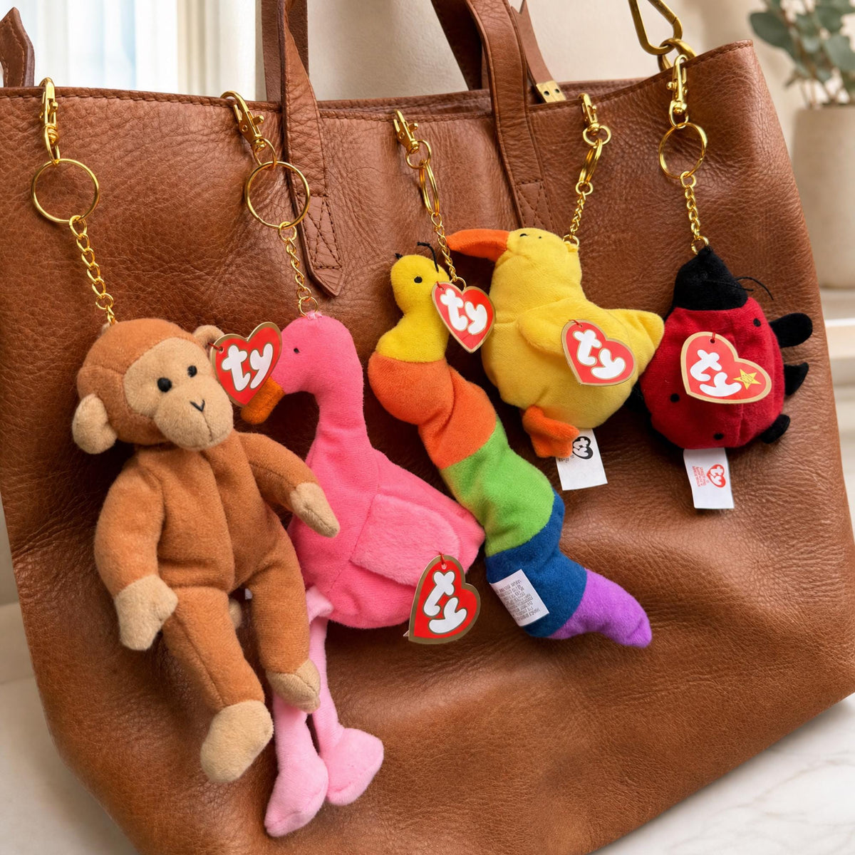 Teenie Beanie Baby bag charms clipped to a brown leather tote bag