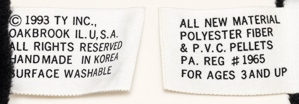 Front and back of a 1st generation tush tag: white fabric with black printing only, a 1993 Ty copyright, Handmade in Korea, and no heart logo or character name.