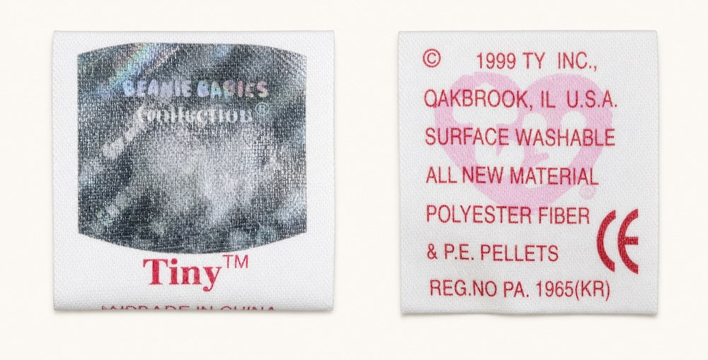 Front and back of a 7th generation tush tag from Tiny, with a metallic hologram in place of the red heart logo and a pink watermark heart on the back.